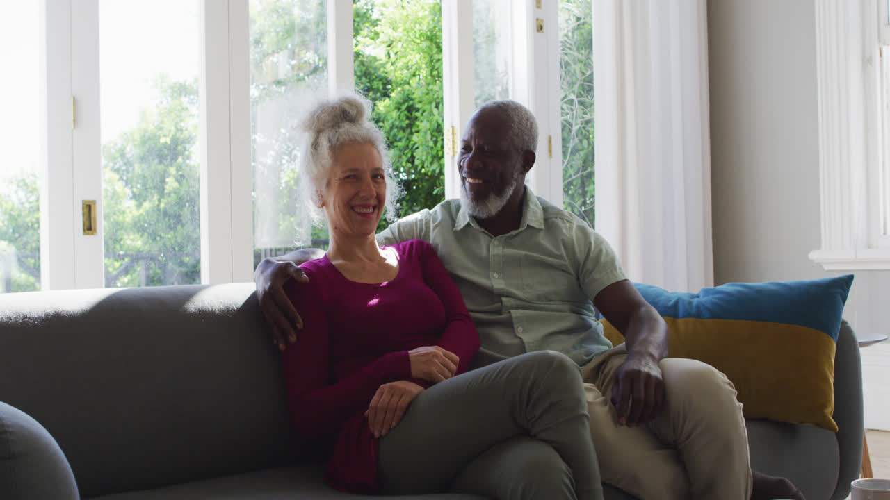Portrait of mixed race senior couple smiling while sitting on the couch at home