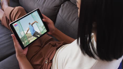 compuesto de una mujer en el sofá en casa viendo un evento de discus de atletismo en una tableta