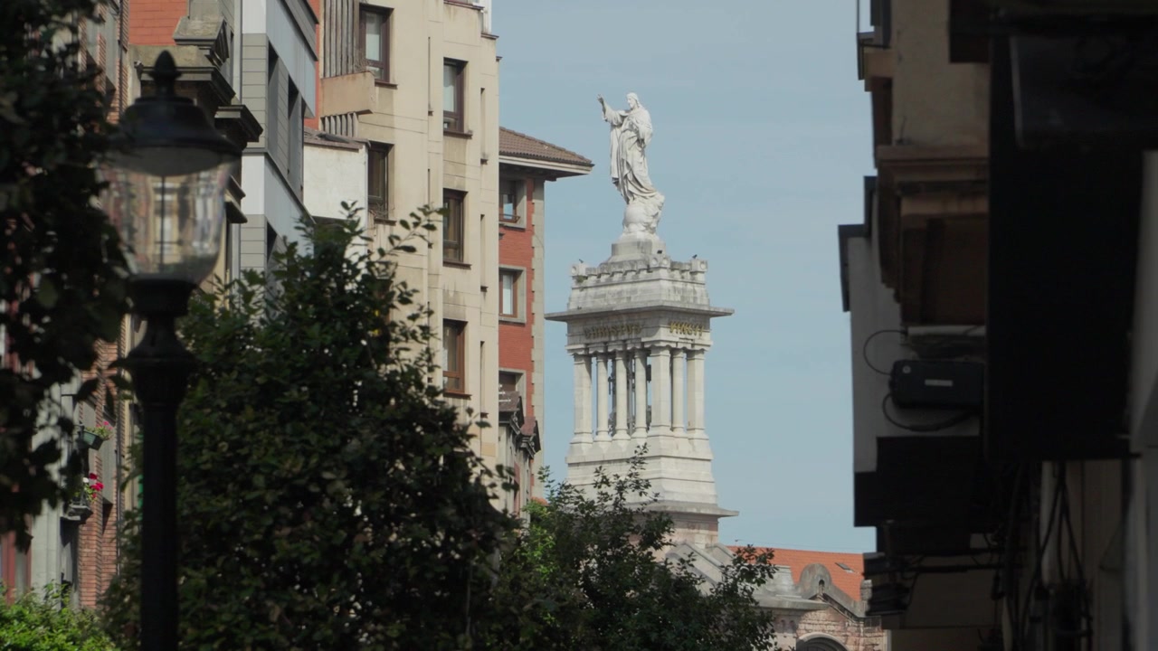 L'iconica statua in marmo bianco di Gesù Cristo in cima alla Basilica del Sacro Cuore che si erge sopra gli edifici stradali a Gijón, Asturie, Spagna