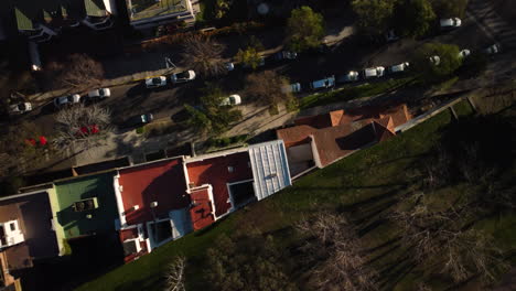 the drone is circling over the house and the road, the house narrows towards the end, sunny, spring, cars are parked along the road