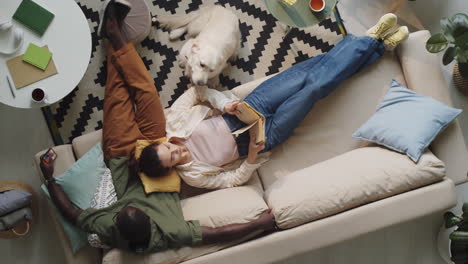 multiethnic couple resting on couch and petting dog at home