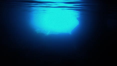 underwater view of the entrance of a sea cave withe the flashy blue light reflecting under the waving surface, vis island, adriatic sea, croatia