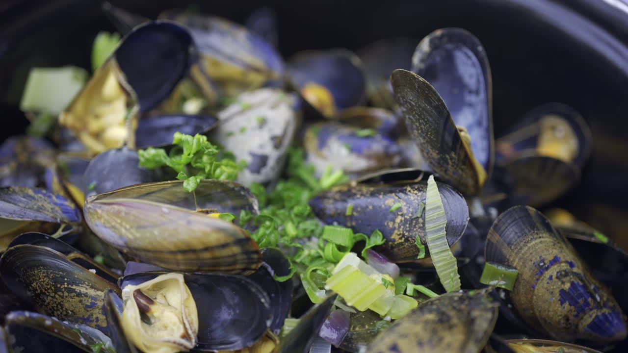 Close up of multiple steamy mussels in a pot with green onions on top