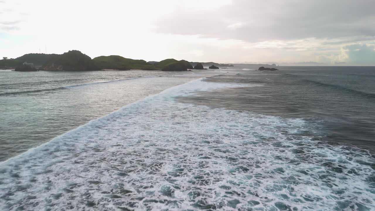 Aerial flies low over shore break surf waves off Kuta Beach on Lombok