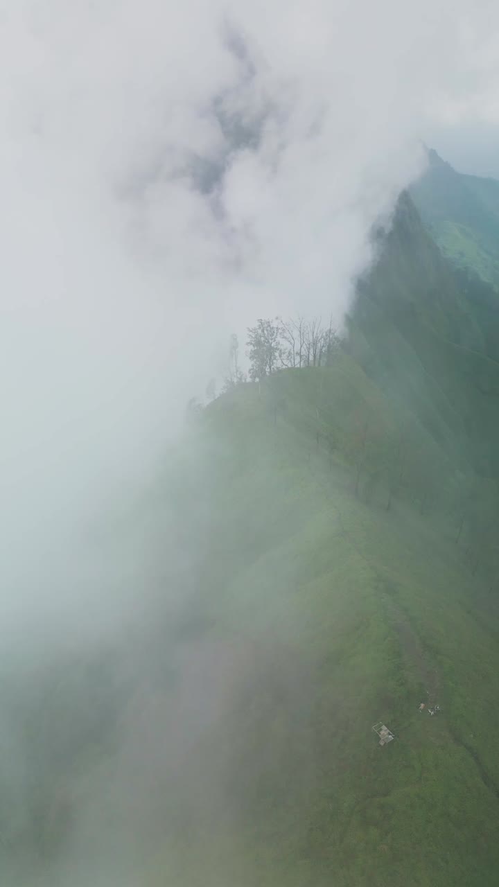 Soaring vertical footage reveals Trunyan Hill covered in clouds, with rolling mist wrapping the green slopes and creating a dramatic highland view of Bali’s scenic mountain landscape