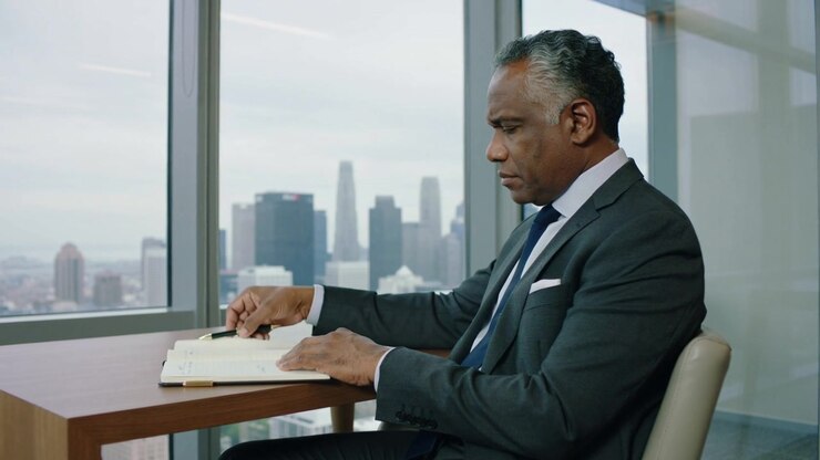 Leaning forward exec checking notebook with pen at office before meeting, skyline, suit, copy space