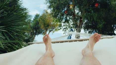 a man is resting in a hammock, a first-person view. in the frame only the legs are visible