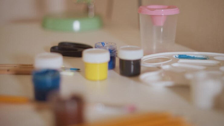 Various paint bottles brushes and craft items arranged on table. scene is softly lit with no human subject visible focusing solely on art supplies materials