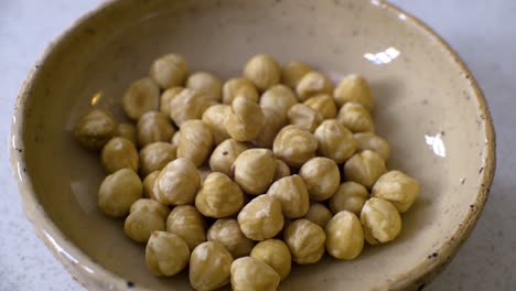 Tiro-De-Avellanas-Peladas-En-Un-Pequeño-Tazón-Beige-Girando-Lentamente