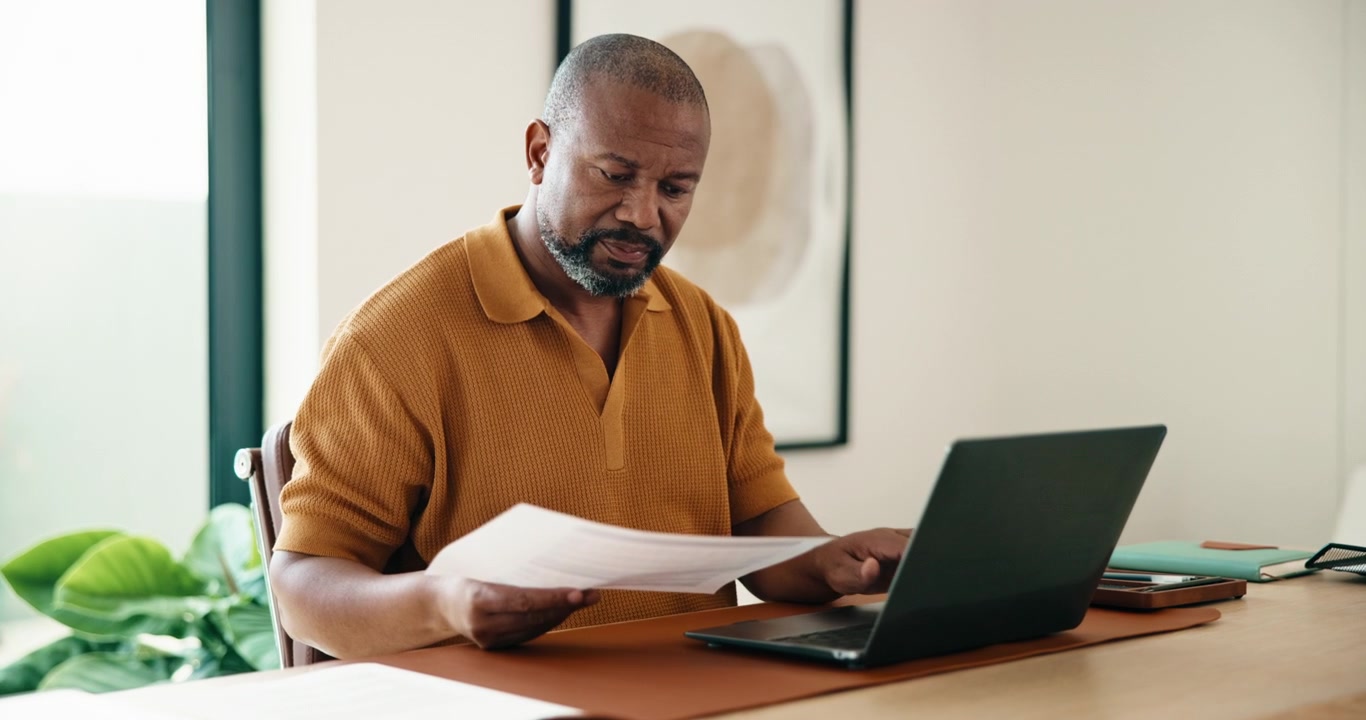 Mature Man Reviewing Documents While Working on Laptop