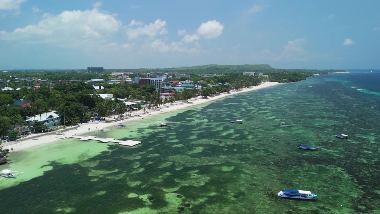 Drone ad alta angolazione si avvicina ad Alona Beach, mostrando acque poco profonde della barriera corallina, barche, sabbia bianca e la costa di Panglao a Bohol
