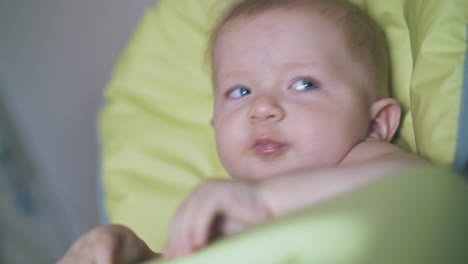 cute baby eats meal sitting in highchair and mother in room