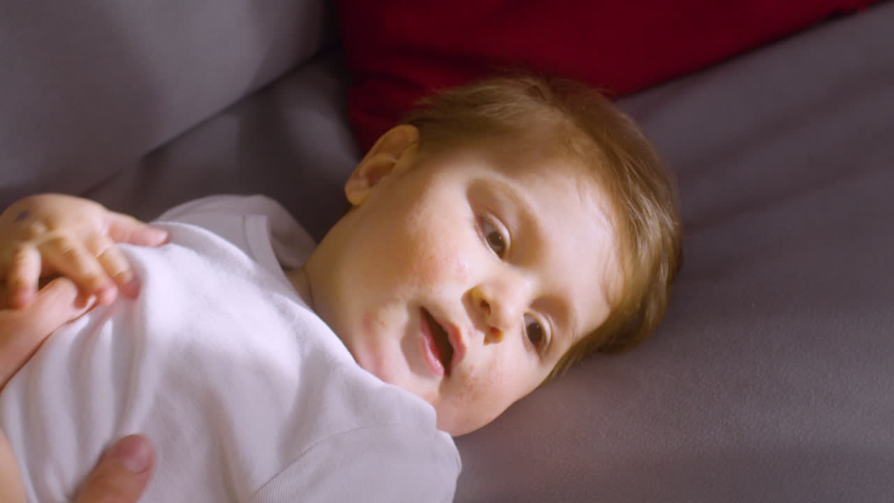 어머니가 간지럽히며 놀고 있는 동안 집에 있는 소파에 누워 웃는 아기의 모습을 가까이서 볼 수 있습니다.