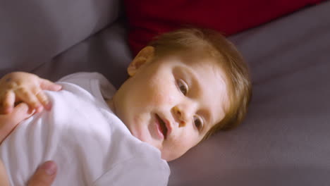 close up view of a smiling baby lying on the sofa at home while his mother tickling and playing with him