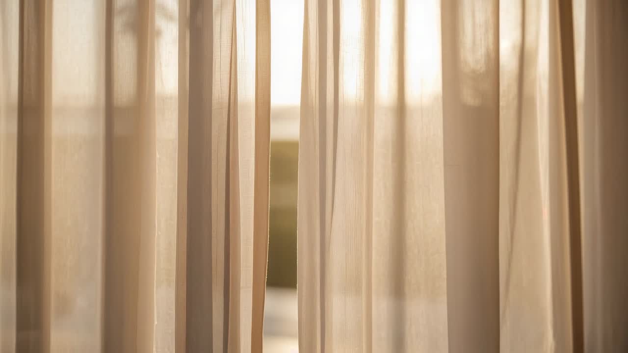 Tende velate beige che scorrono alla finestra in risposta alla luce solare cangiante, rivelando un fogliame sfocato.