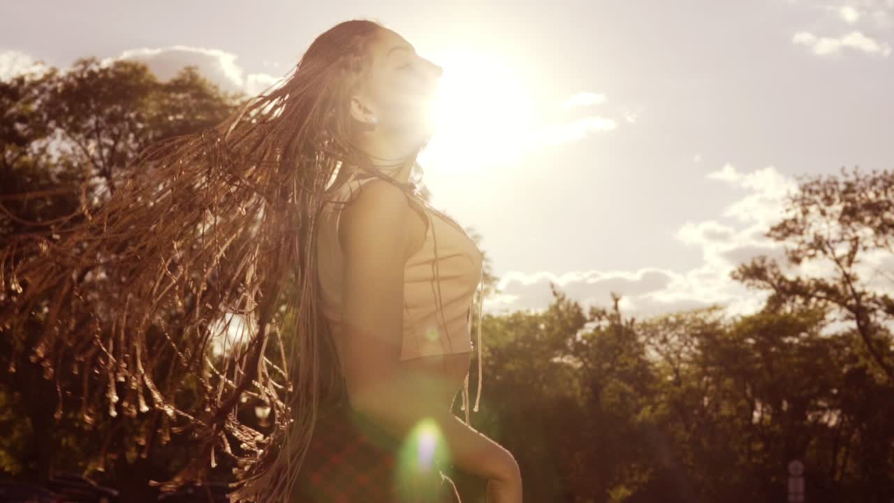 Beautiful woman with dreads styling hair and shaking her head in the son. Happy calm attractive girl with long dreads having fun