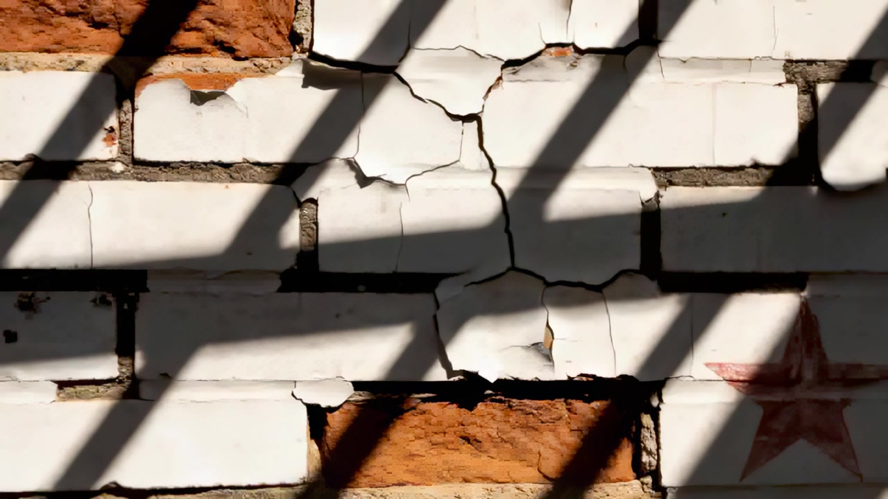 Shifting sun moving shadows through slats across brick wall, exposing peeling paint and red star