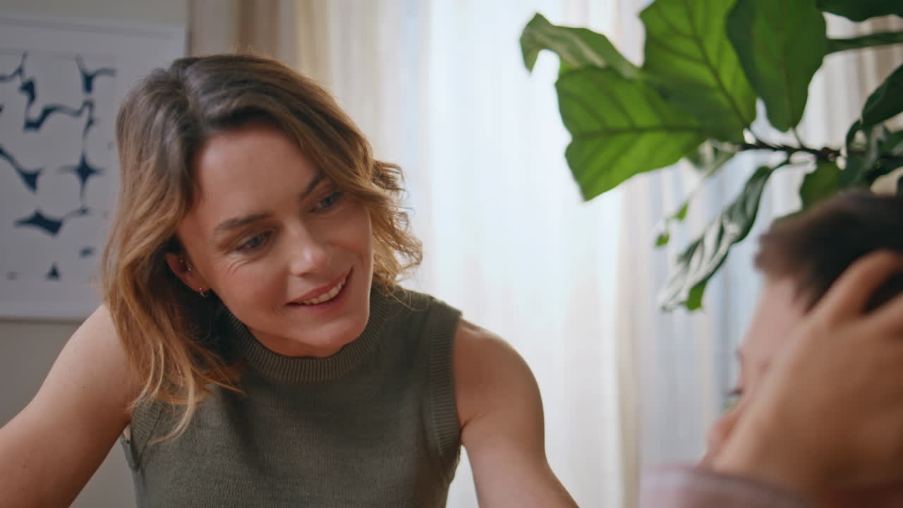 Smiling mother talking child at greenery living room closeup. Woman stroking son