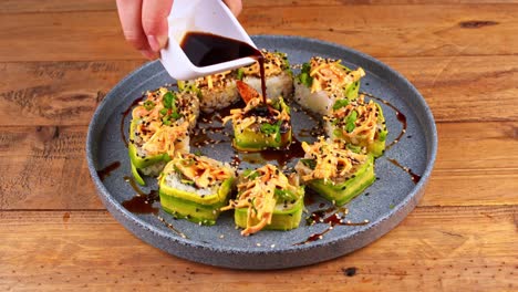 Close-up-of-a-plate-of-avocado-sushi-that-is-bathed-in-Worcestershire-sauce,-but-only-in-the-center-on-a-blue-plate-on-a-wooden-table-in-a-restaurant