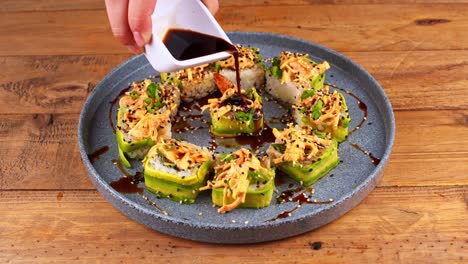 primer plano de un plato de sushi de aguacate que está bañado en salsa de worcestershire, pero sólo en el centro en un plato azul en una mesa de madera en un restaurante