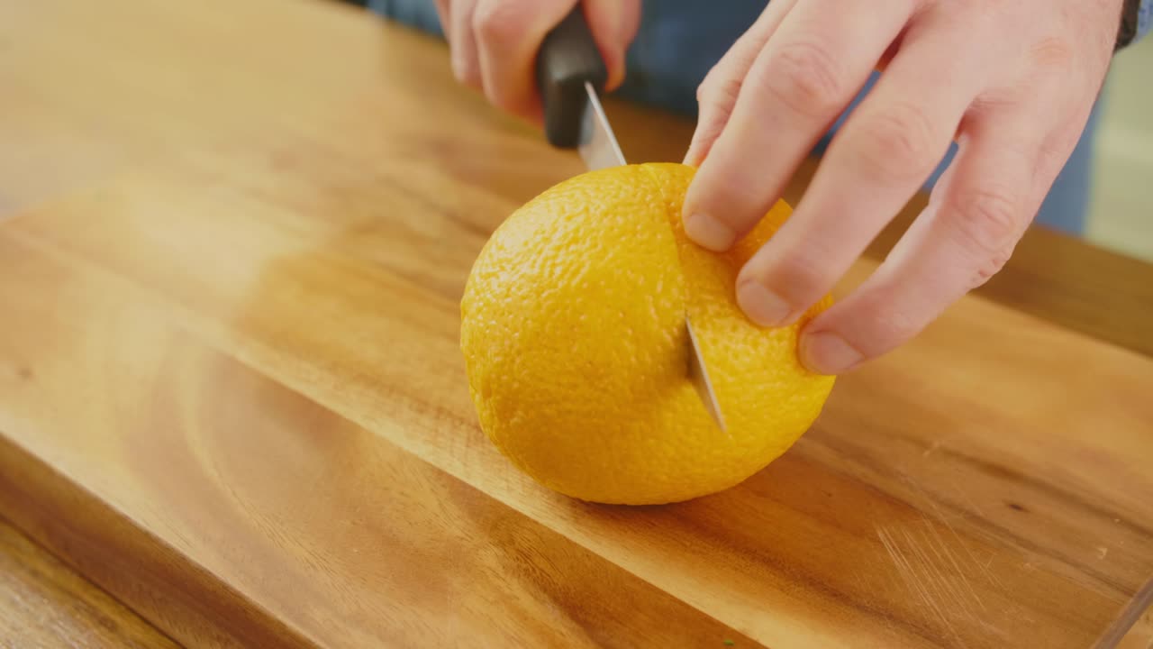 Man's Hands Cutting Whole Orange With Knife On Chopping Board