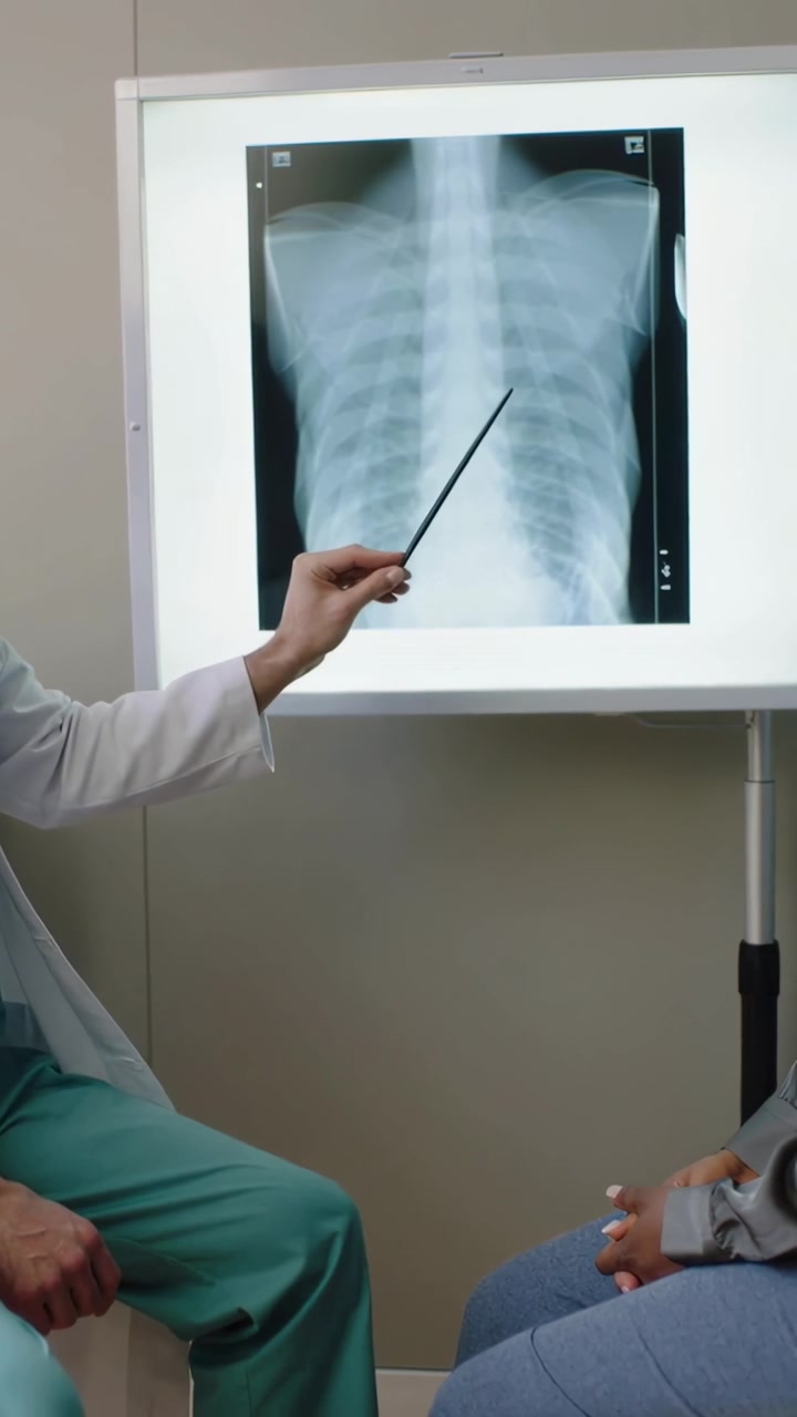 Vertical video: Starting review doctor in coat pointing with rod across xray in exam room