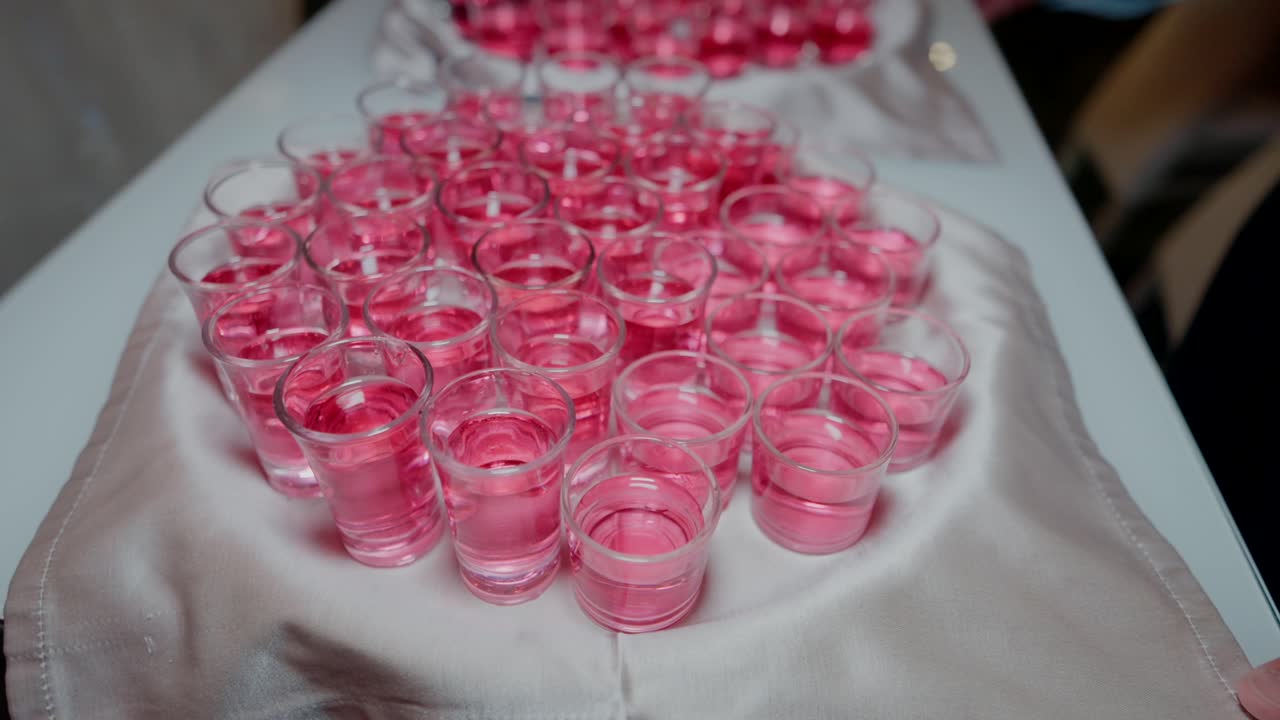 Tray of small pink shot glasses arranged on a white cloth, ready for serving.