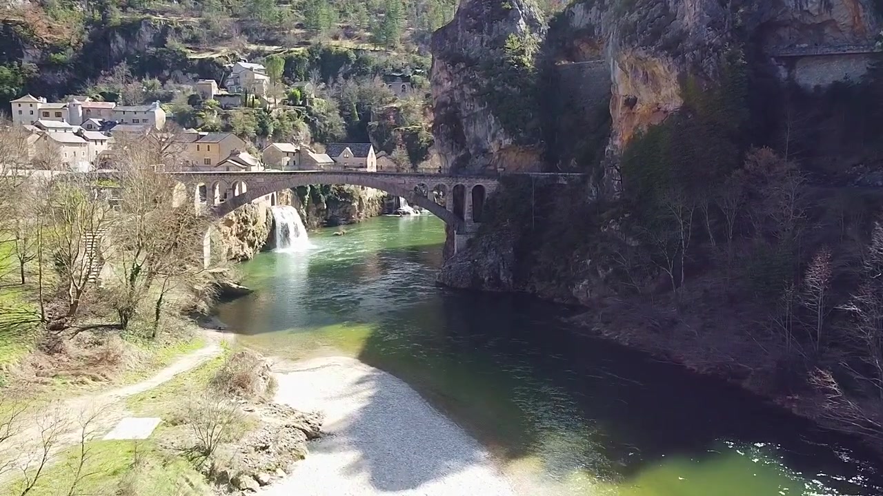 Ponte sul fiume e le cascate di Saint-Chély-Du-Tarn. Vista aerea ravvicinata. Gole del Tarn. Cascata. Cascata accanto a case in pietra lungo il fiume. Francia.