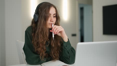 concertrated student girl in headphones has distant lesson on laptop, making notes