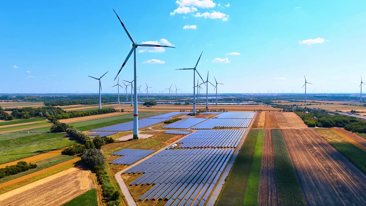 Solcelleanlæg og vindmøller på landet. Fugleperspektiv af en moderne energipark placeret nær afgrøder og træer.