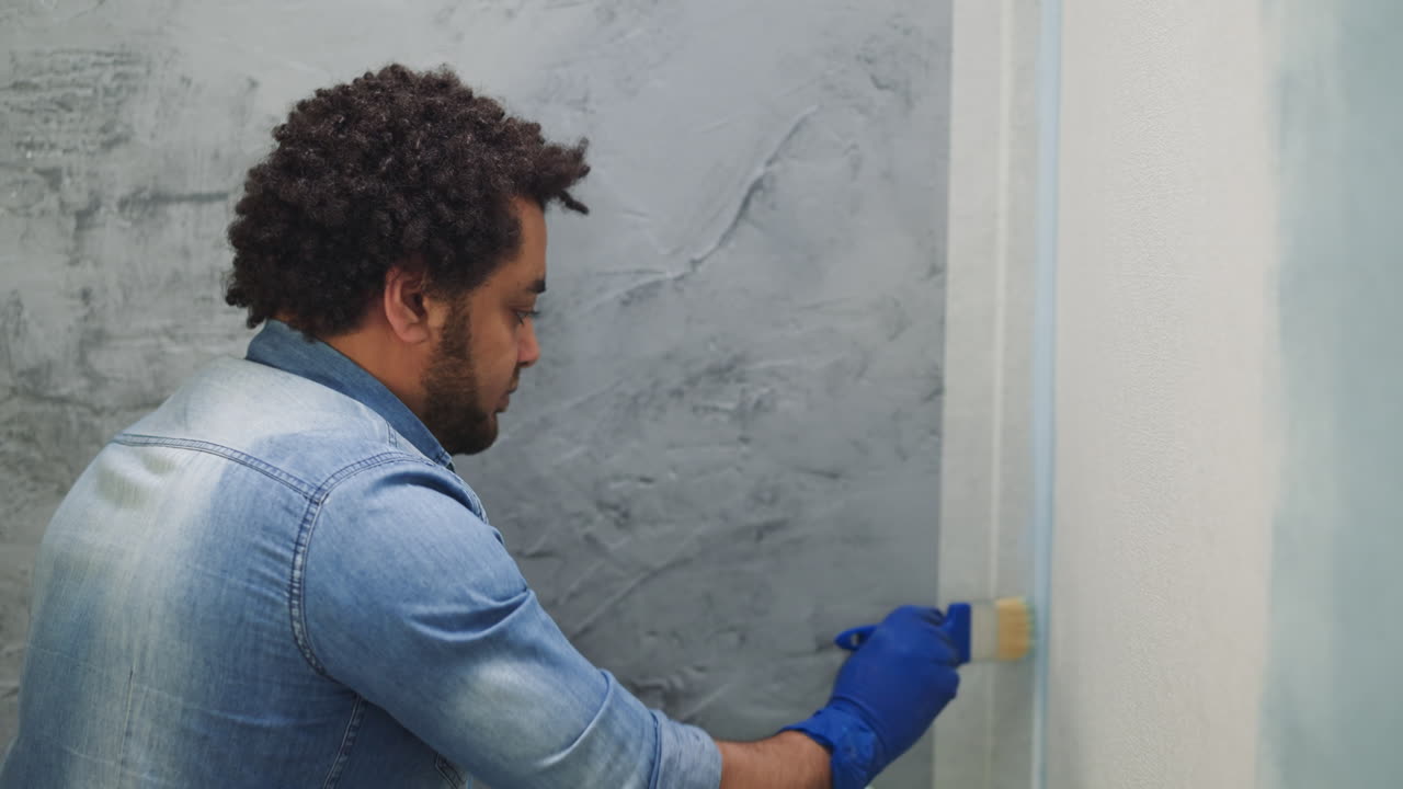 hombre negro en camisa de denim pinta la esquina con pincel en la habitación