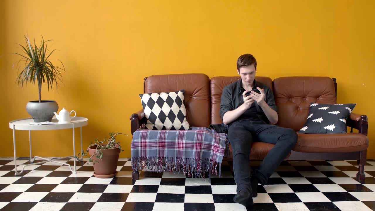 사람 은 거실 에 있는 소파 에 휴대 전화 를 사용 하고 있다