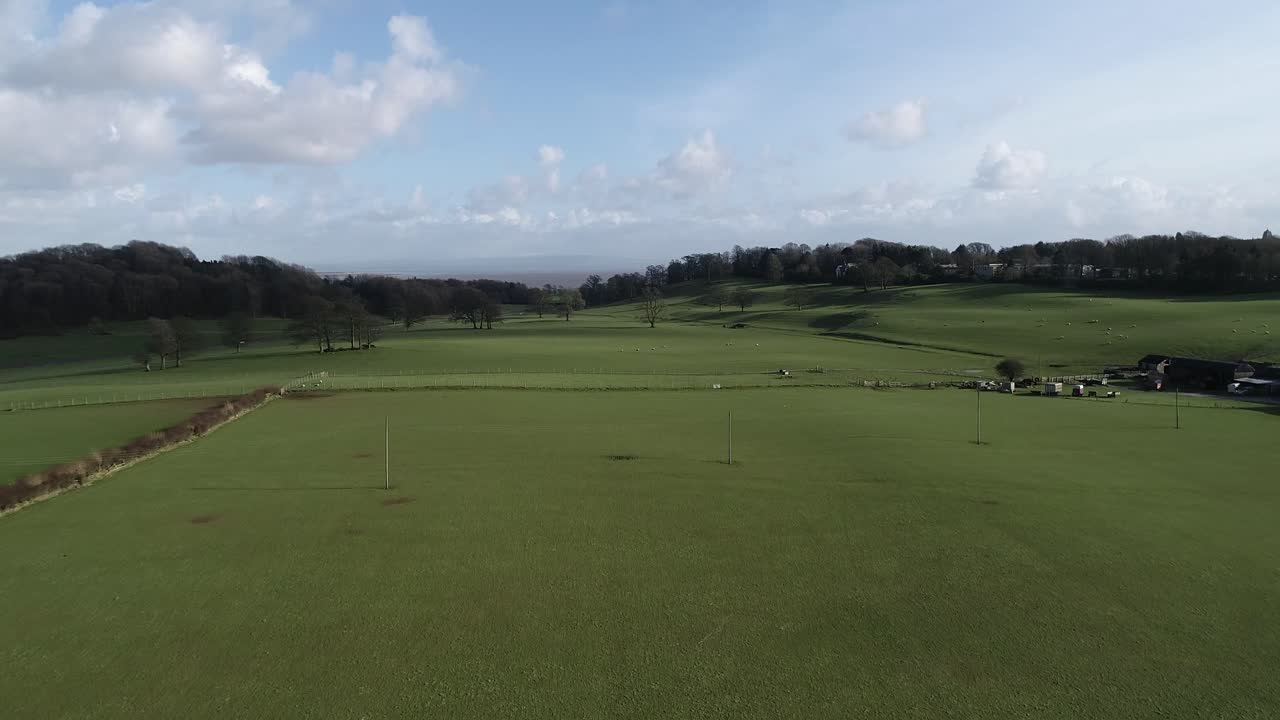 Drone flight over Ulverston across pasture fields towards hills providing an aerial view of an empty meadow.