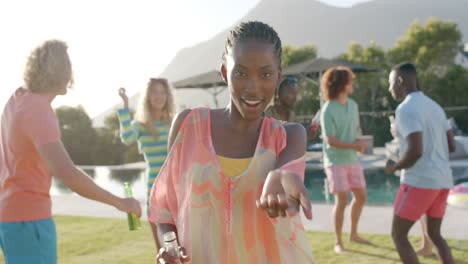 feliz mujer afroamericana con bebida y diversos amigos bailando en una piscina soleada fiesta, cámara lenta