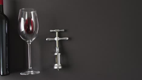 red wine glass and corkscrew lying on black surface with copy space