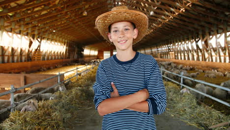 portrait of caucasian teen boy in hat looking at camera in stable with sheep flock