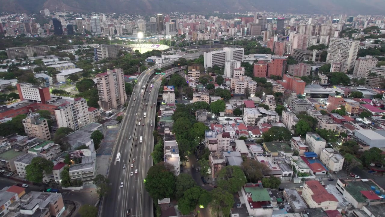 Vista dall'alto di auto che percorrono un'autostrada urbana circondata da edifici residenziali e montagne durante l'ora d'oro.