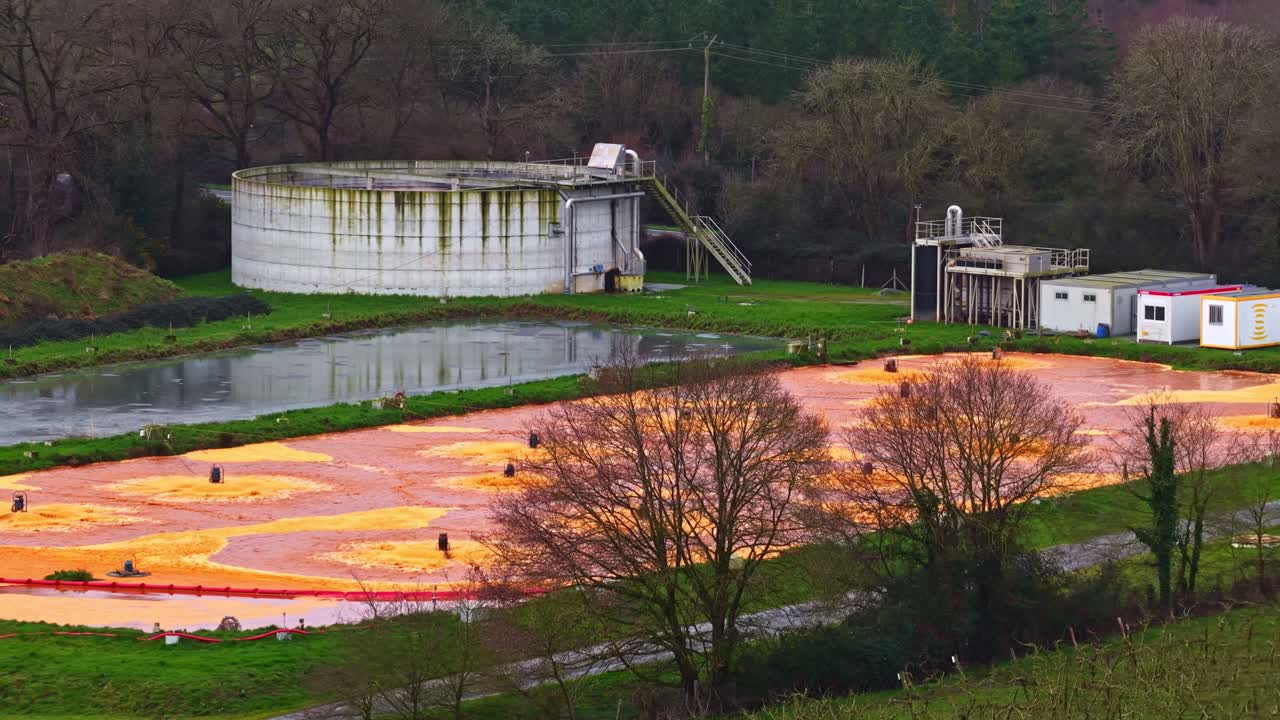 Vista aerea di colorati stagni di ossidazione giallo-arancio con aeratori galleggianti presso un impianto di trattamento delle acque reflue, circondato da foreste e serbatoi in un sito industriale rurale