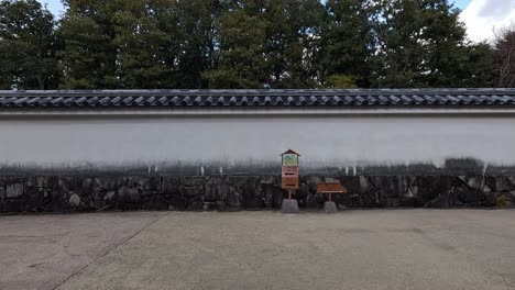 Stone-lined walkway between white walls at Himeji Castle, Japan, with tiled roofs and trees in the background.