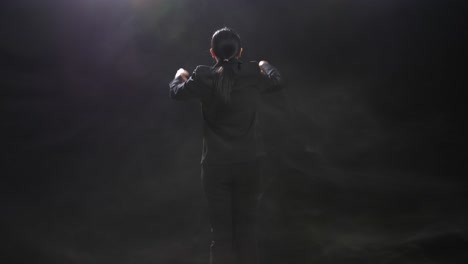 back view of asian conductor woman holding a baton and showing gesture quickly in the black studio with fog