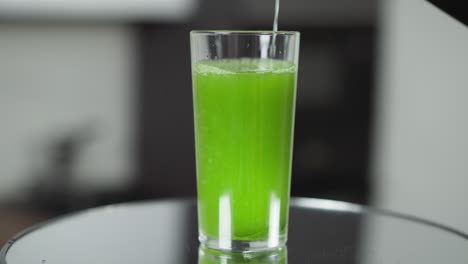 water pouring into a tall glass, mixing with green juice, creating a refreshing drink