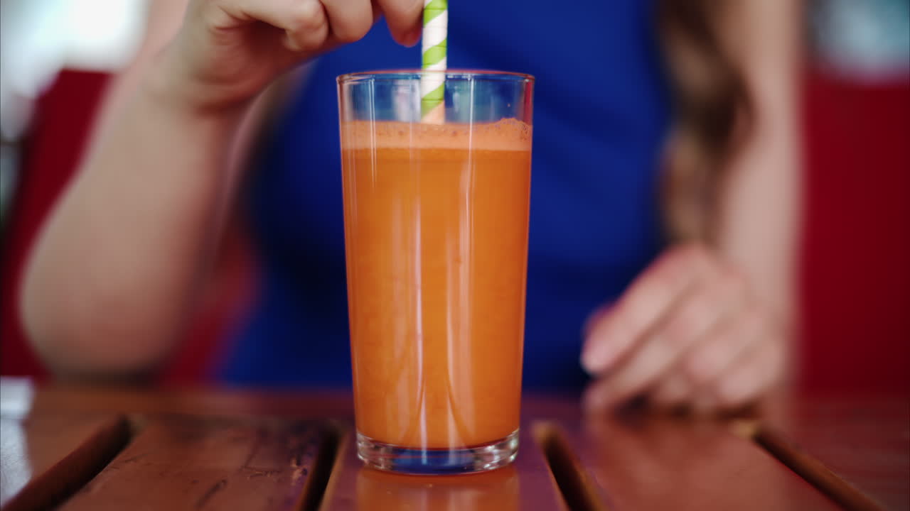 Woman in a blue dress mixing a carrot juice with a straw at a restaurant