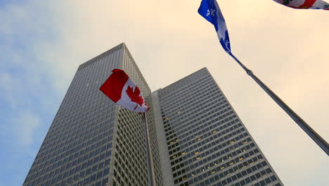 Low-angle-shot-of-a-high-skyscraper-tower-,-canada-and-Quebec-flags-and-beautiful-sky-and-clouds