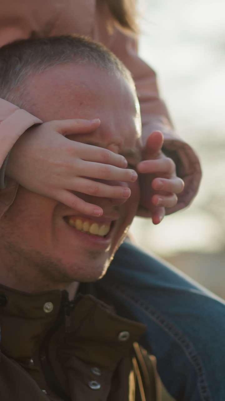 padre sonriendo con su hija jugando con su cara en el parque durante la puesta del sol, ambos riendo alegremente