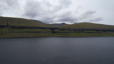 aerial over eysturoy fjord to fossa waterfall in streymoy island, drifting clouds