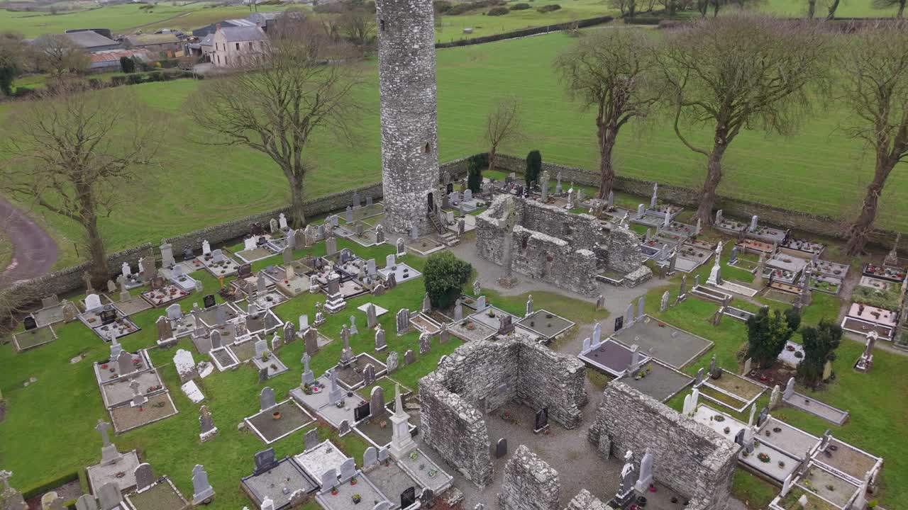 Round Tower, High Cross, Church, And Gravestones At Monasterboice Ruins In County Louth, Ireland. - aerial shot