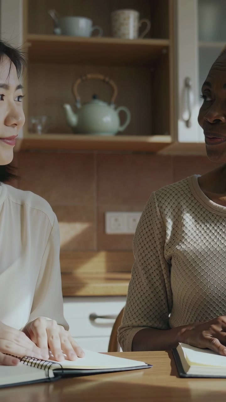 Vertical video: Flipping notebook, 2 women in blouse, sweater glancing in kitchen while studying