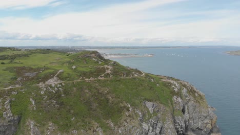 Aerial-footage-of-large-mountain-with-people-walking-and-trekking-on-it-near-blue-sea-and-ocean-on-a-bright-and-blue-sunny-day