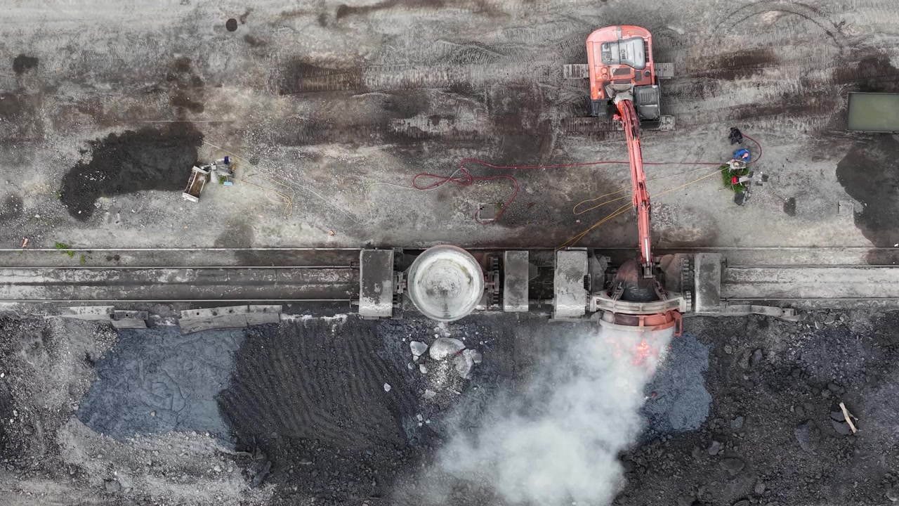 Un escavatore versa metallo fuso in un'unità di lavorazione in un cantiere industriale impegnativo.