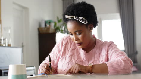 african american woman writes in a notebook at a desk at home